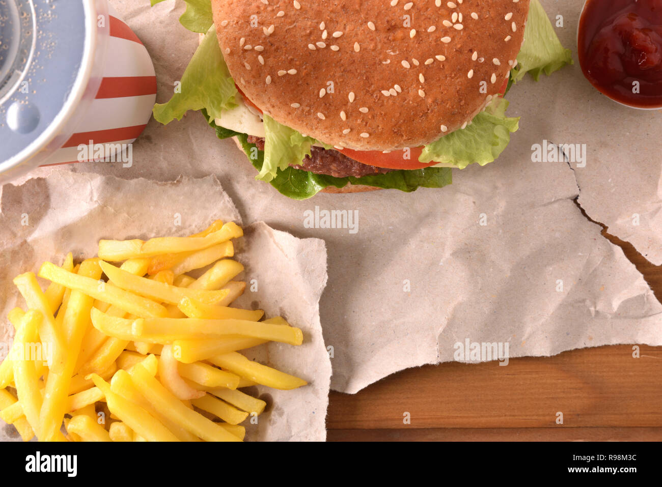 Hamburger di manzo con formaggio e pomodori su carta con chip su un tavolo di legno. Vista dall'alto. Composizione orizzontale. Foto Stock