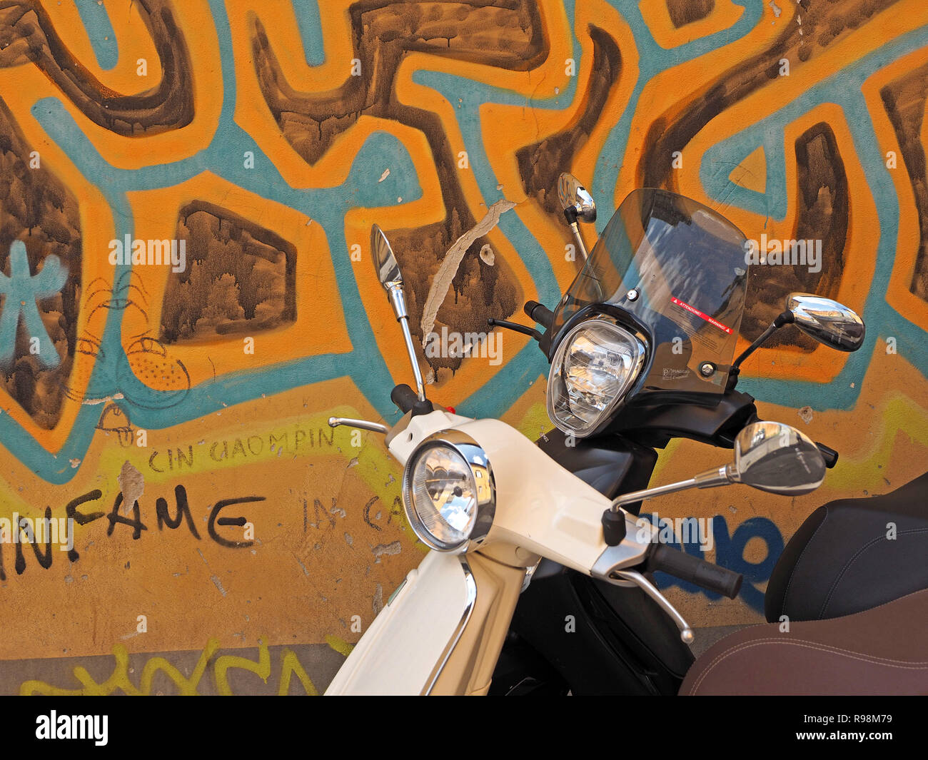 Due Vespa scooter uno nero 1 bianco parcheggiato a fianco a fianco contro il drammatico, mazy blu e oro graffiti dipinti in una strada della città di Pisa, Italia Foto Stock