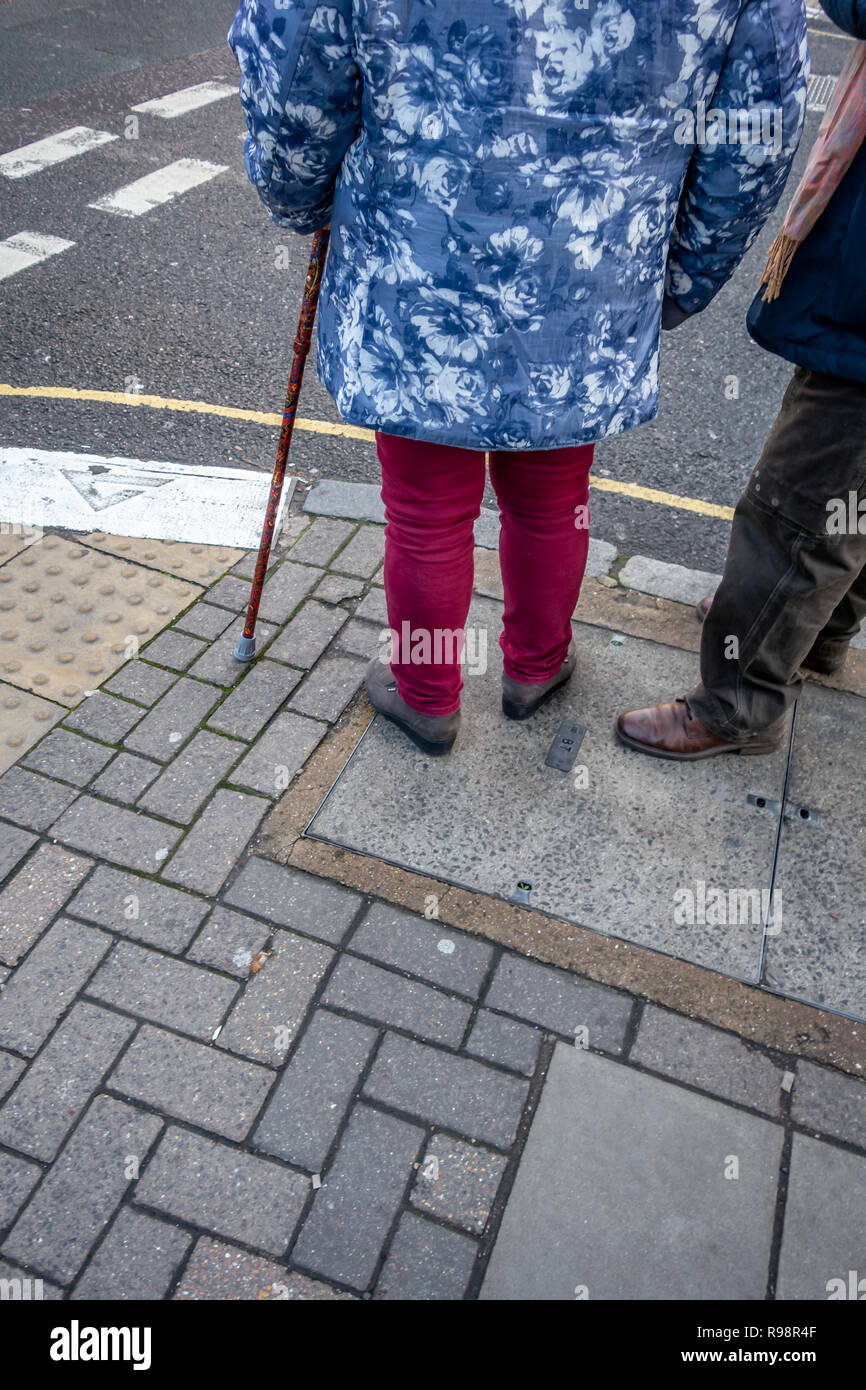 Il corpo inferiore solo del vestito eccentricamente anziano uomo e donna con l'aiuto di una canna in attesa di attraversare una strada a Londra Foto Stock