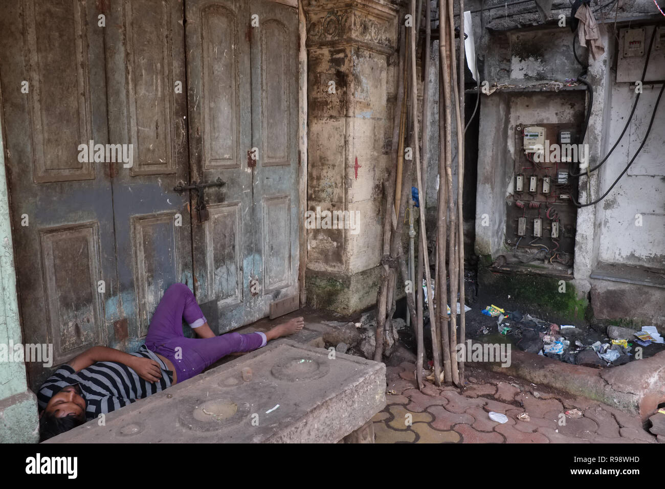 Un uomo dorme in un portale in Mumbai, India, accanto a per una dubbia cercando unità elettrica contatore e trasformatore Foto Stock