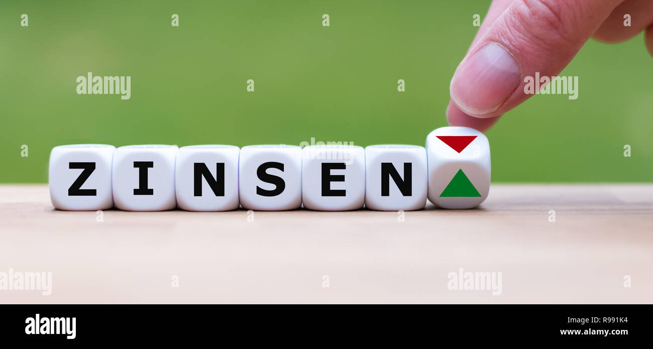 È a mano ruotando un dado e cambia la direzione di una freccia che simboleggia che i tassi di interesse ("Zinsen' in tedesco) stanno andando su (o viceversa) Foto Stock