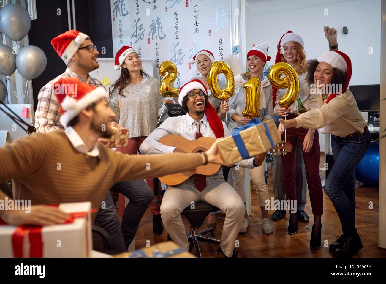 Sorridente lavoratori aziendali hanno divertimento e balli in Santa hat alla festa di Natale e scambio di doni in office Foto Stock
