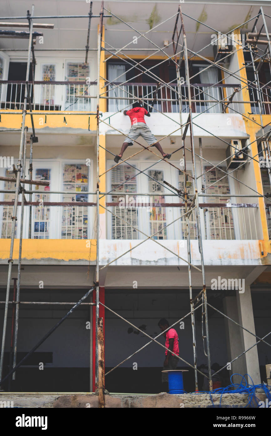 Operaio edile esemplifica il concetto di rischio professionale mentre si lavora su una impalcatura alta, Sri Lanka Foto Stock