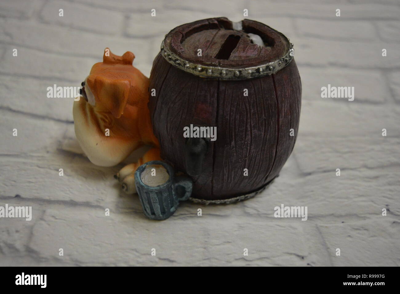 Vassoio antigoccia in ceramica sotto forma di botte di birra con testa di cane e un bicchiere di birra blu accanto sullo sfondo di una parete di mattoni bianchi. Foto Stock