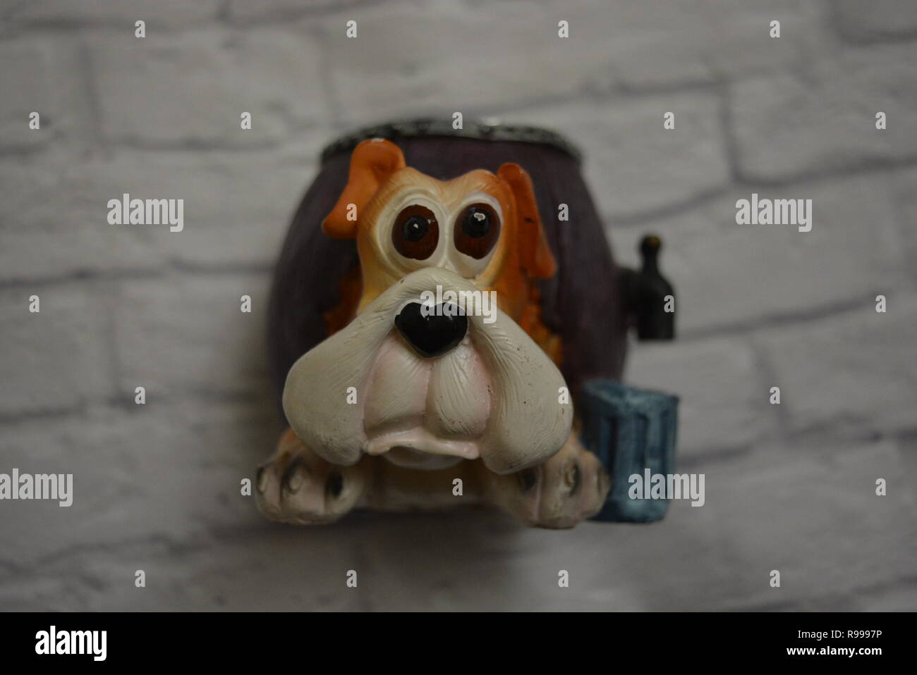 Vassoio antigoccia in ceramica sotto forma di botte di birra con testa di cane e un bicchiere di birra blu accanto sullo sfondo di una parete di mattoni bianchi. Foto Stock