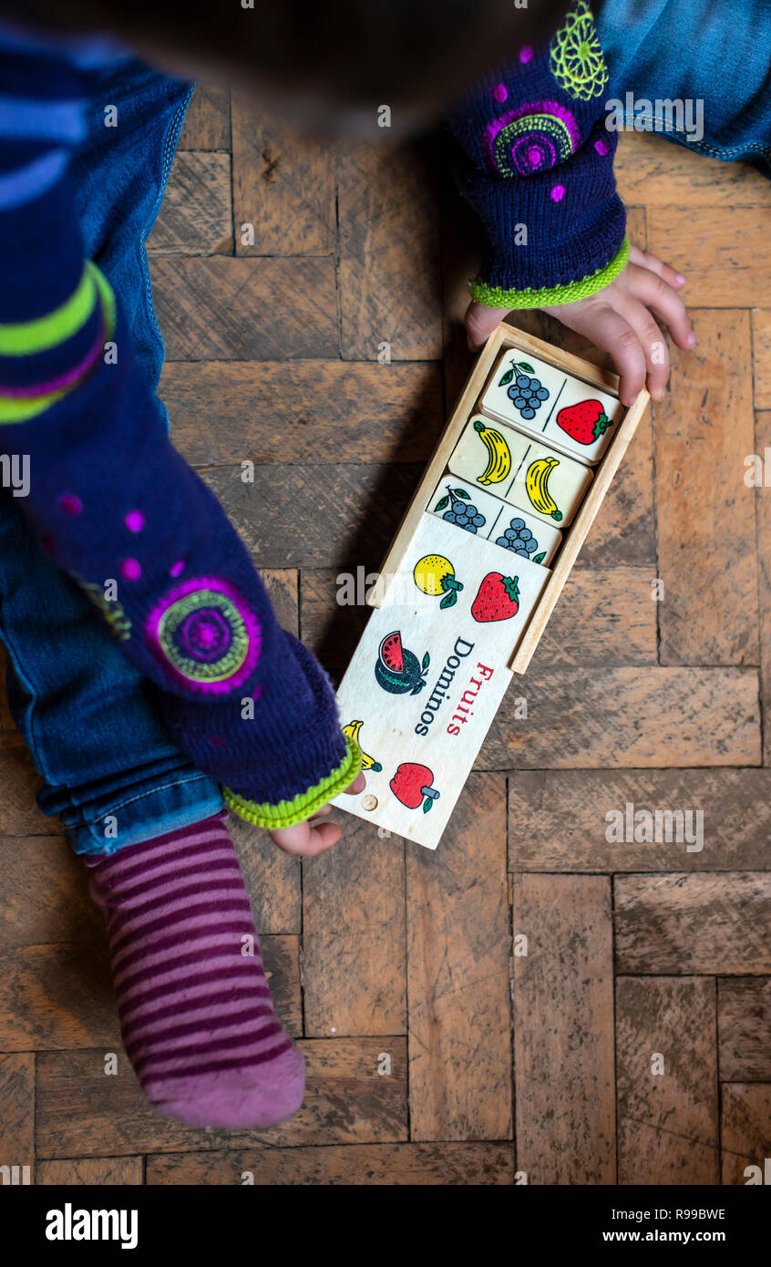 Bambini che giocano con frutti dipinta su blocchi di legno. Bambina gioca sul pavimento a casa. Frutti metafora concettuale. Foto Stock