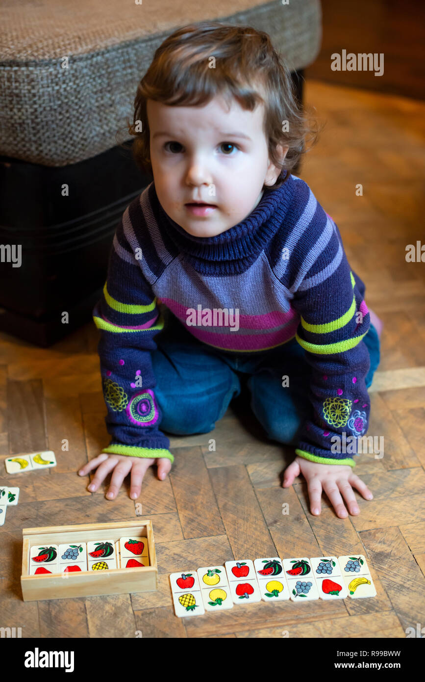 Bambini che giocano con frutti dipinta su blocchi di legno. Bambina gioca sul pavimento a casa. Frutti metafora concettuale. Foto Stock
