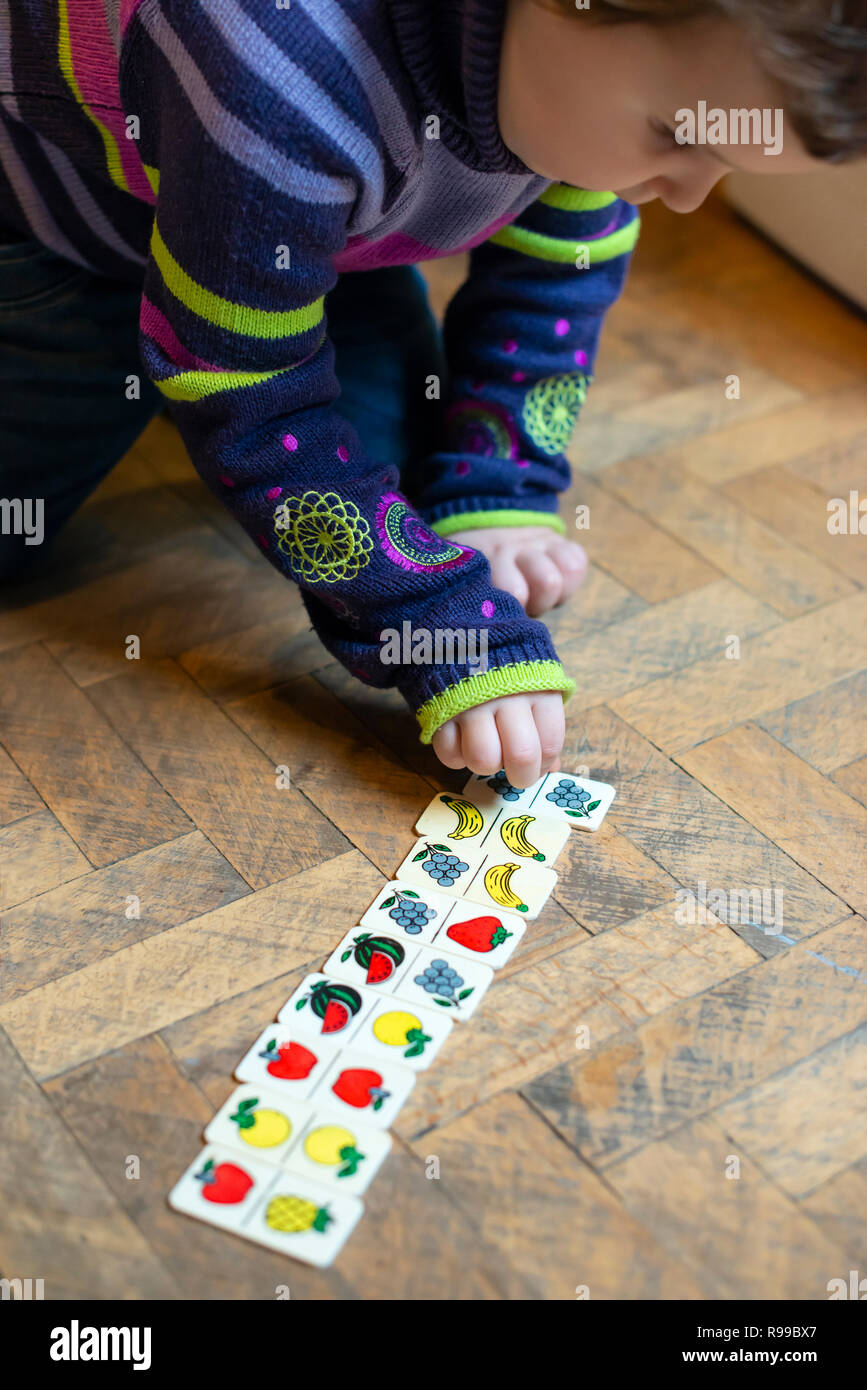 Bambini che giocano con frutti dipinta su blocchi di legno. Bambina gioca sul pavimento a casa. Frutti metafora concettuale. Foto Stock