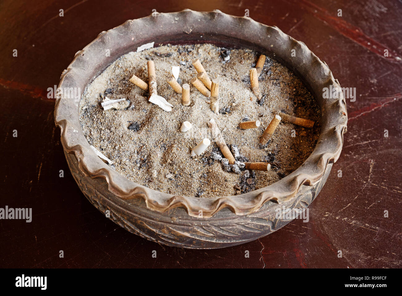 Di grandi dimensioni in ceramica posacenere con sabbia e mozziconi di sigaretta su un tavolo di legno Foto Stock