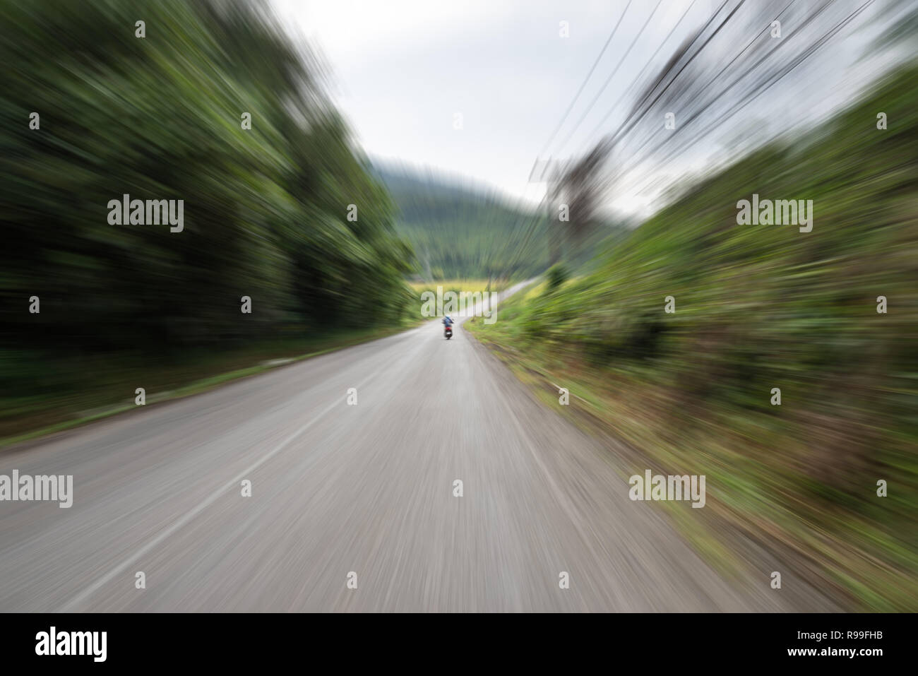 Vista da dietro uno scooter su una strada in Laos con motion blur che mostra la velocità Foto Stock