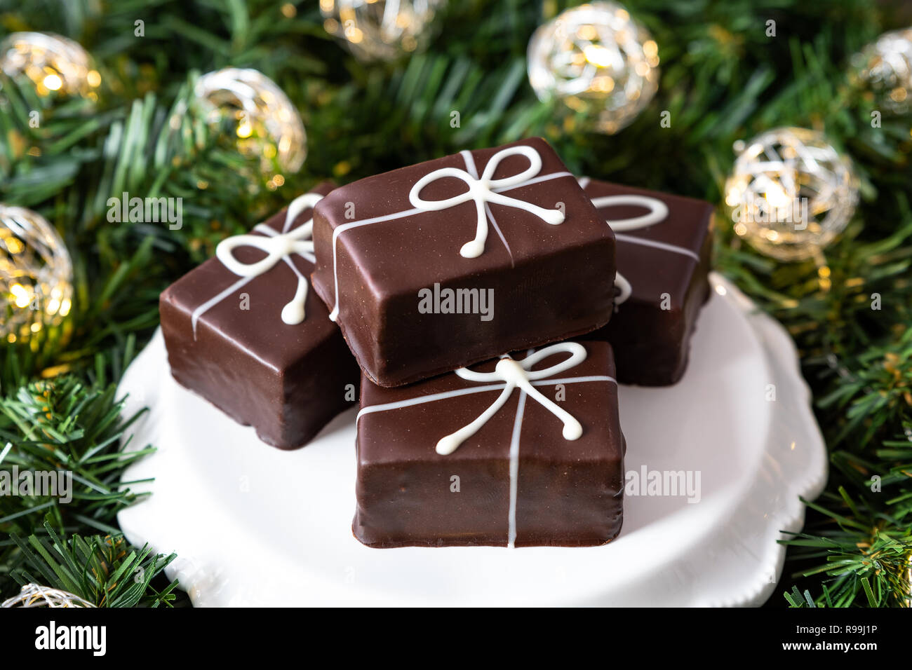 Singoli regalo di Natale torte al cioccolato su una piastra bianca, in una corona di fiori con LED luci di Natale su uno sfondo di legno Foto Stock