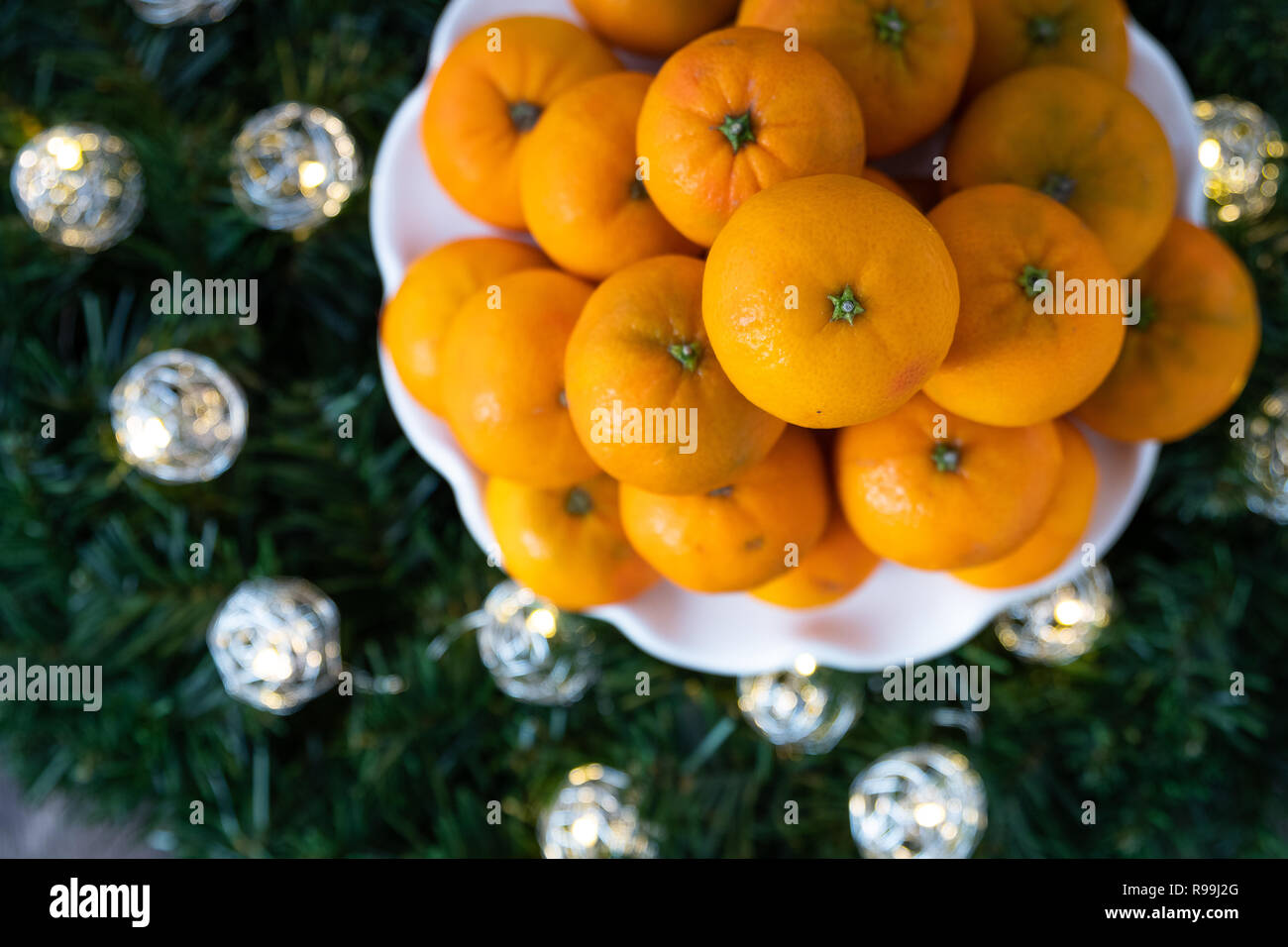 Pila di arance satsuma su una piastra bianca, in una corona di fiori con LED luci di Natale su uno sfondo di legno Foto Stock