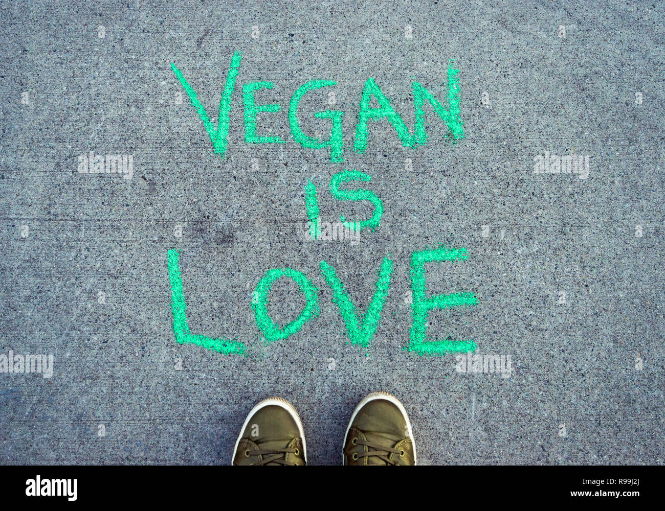 Parole di testo vegane è Amore in verde chalk scritte sul marciapiede di cemento con POV verde scarpe casual. Foto Stock