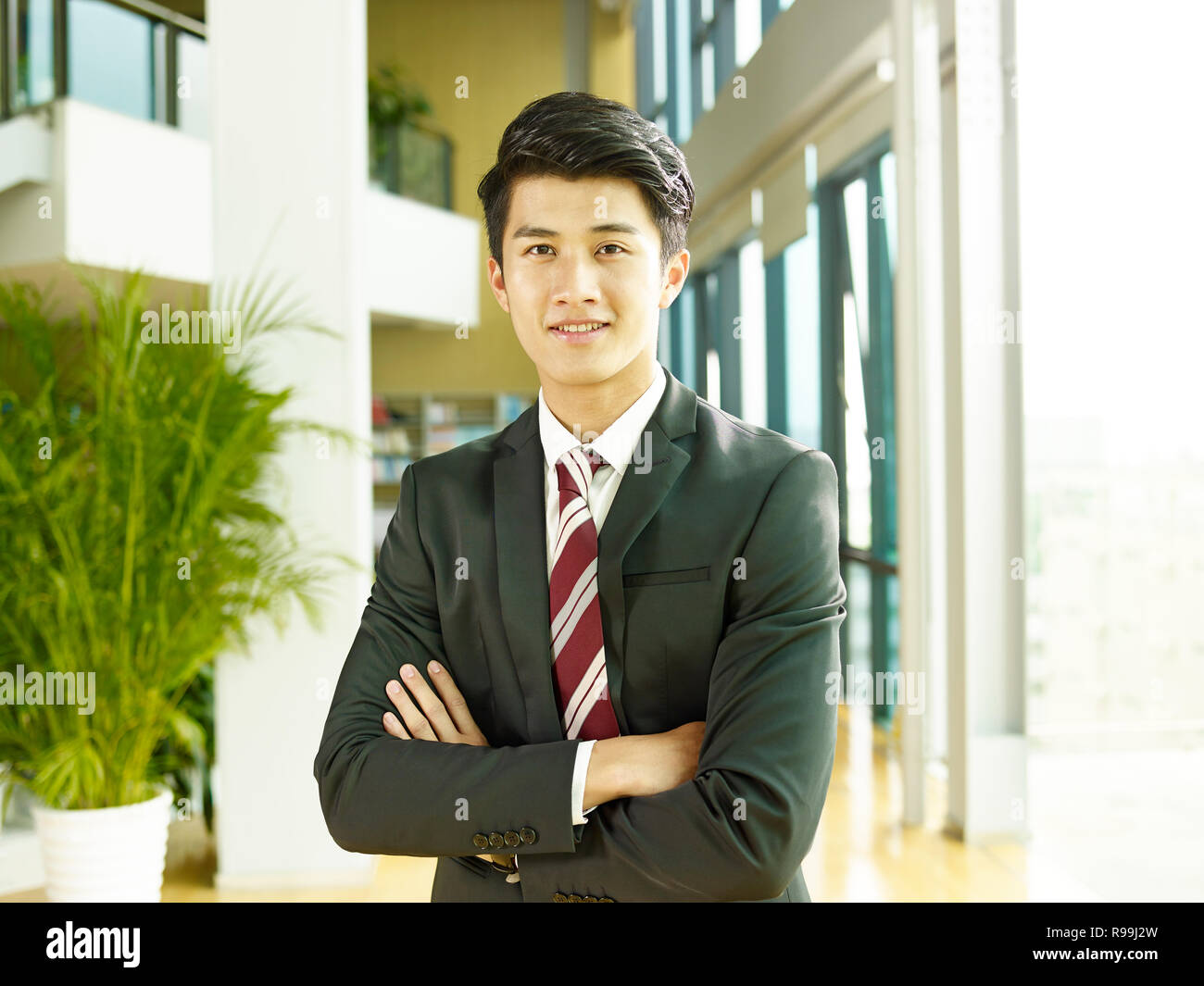 Ritratto di un giovane asian business man, con le braccia incrociate, guardando la telecamera sorridendo. Foto Stock