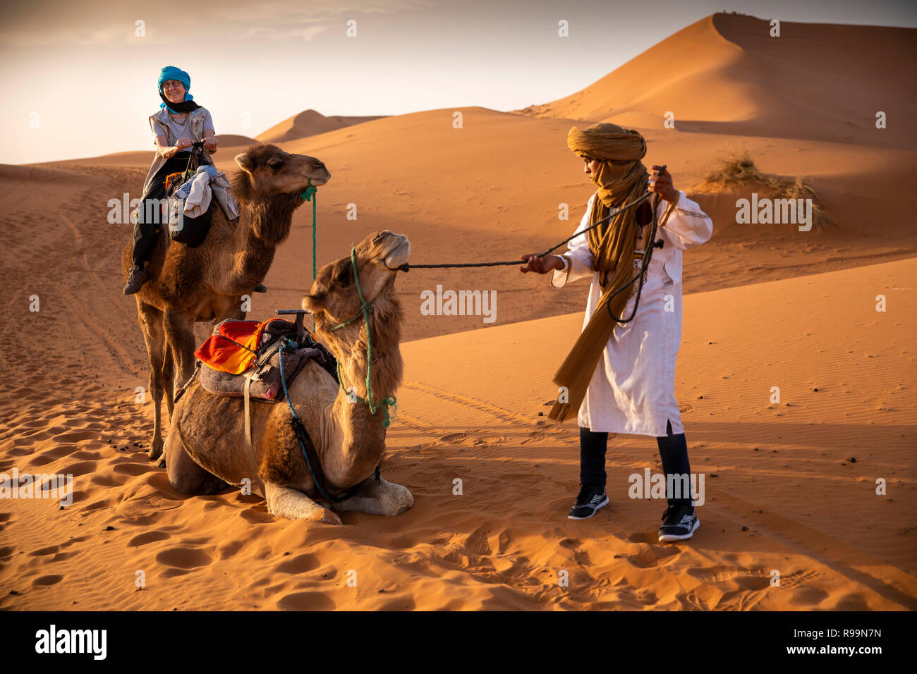 Il Marocco, Errachidia Provincia, Erg Chebbi, Guida Berber sollevamento cammello su corsa attraverso le dune Foto Stock