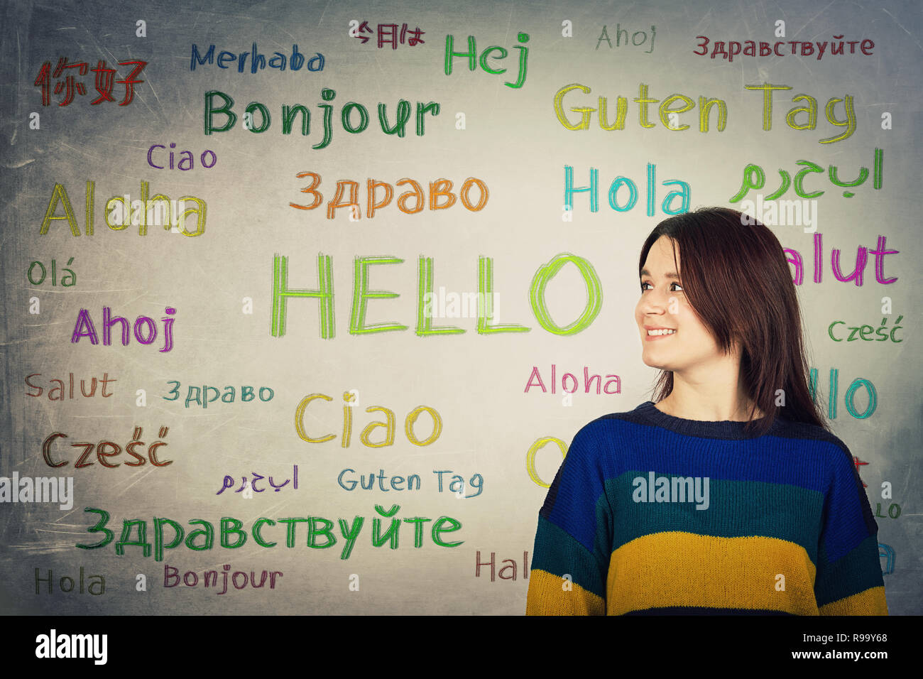 Ragazza piuttosto di fronte a una lavagna scritto con la parola hello in diverse lingue e colori. Opportunità per imparare tante lingue per studen Foto Stock