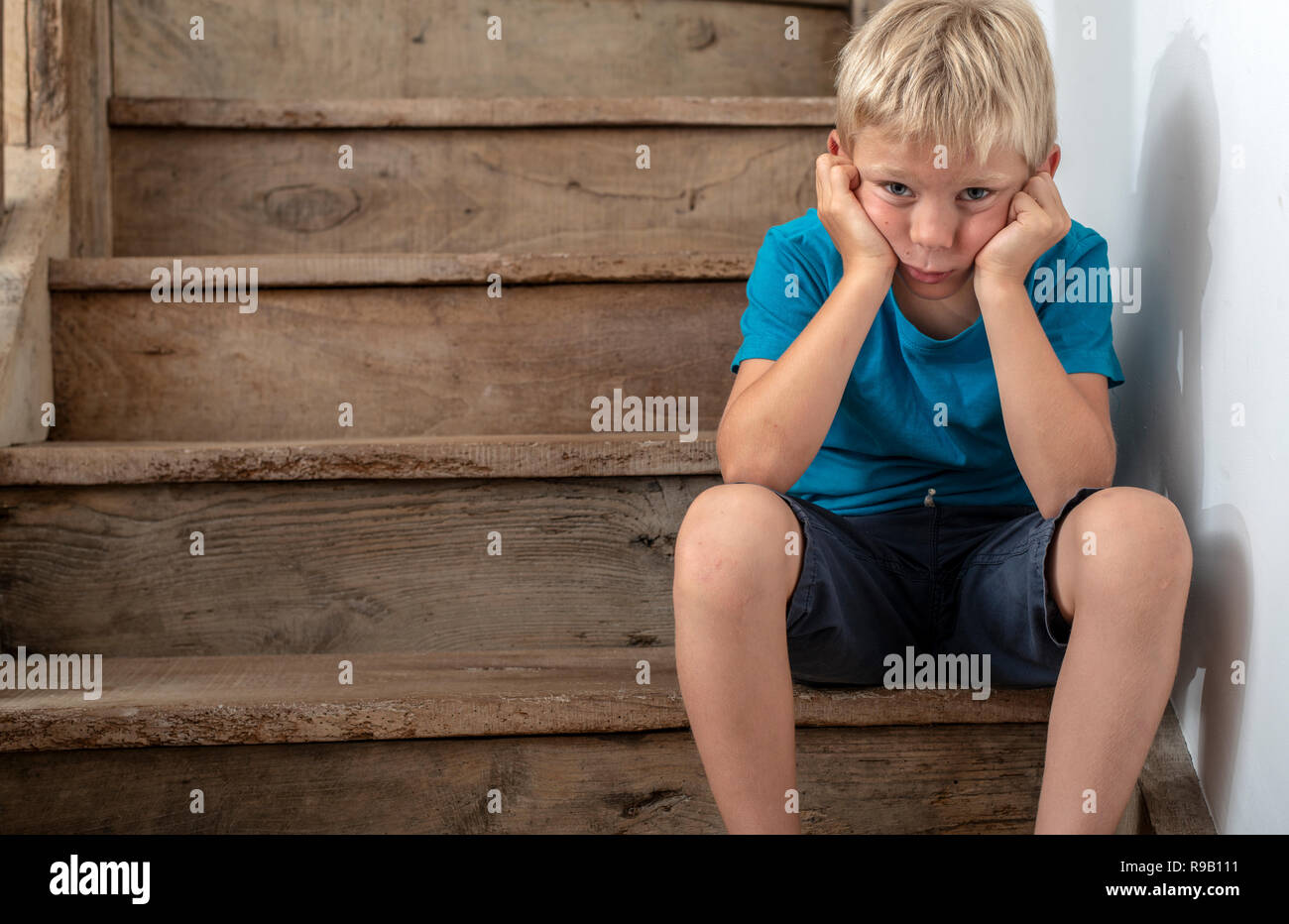 Bambino seduto sulle scale in naughty corner, adirato o triste. Foto Stock