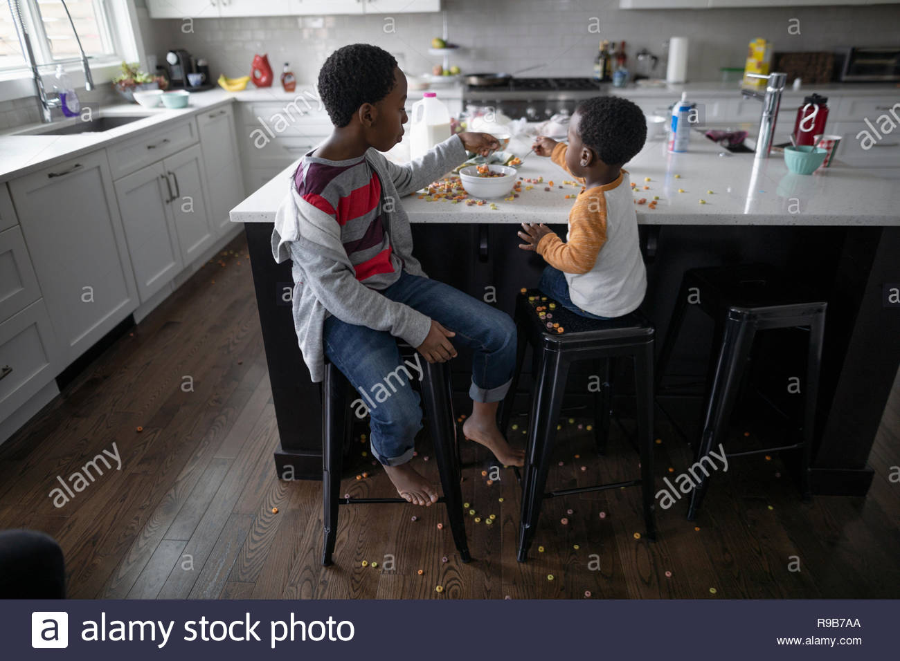 Fratelli disordinati mangiare cereali a Isola per cucina Foto Stock
