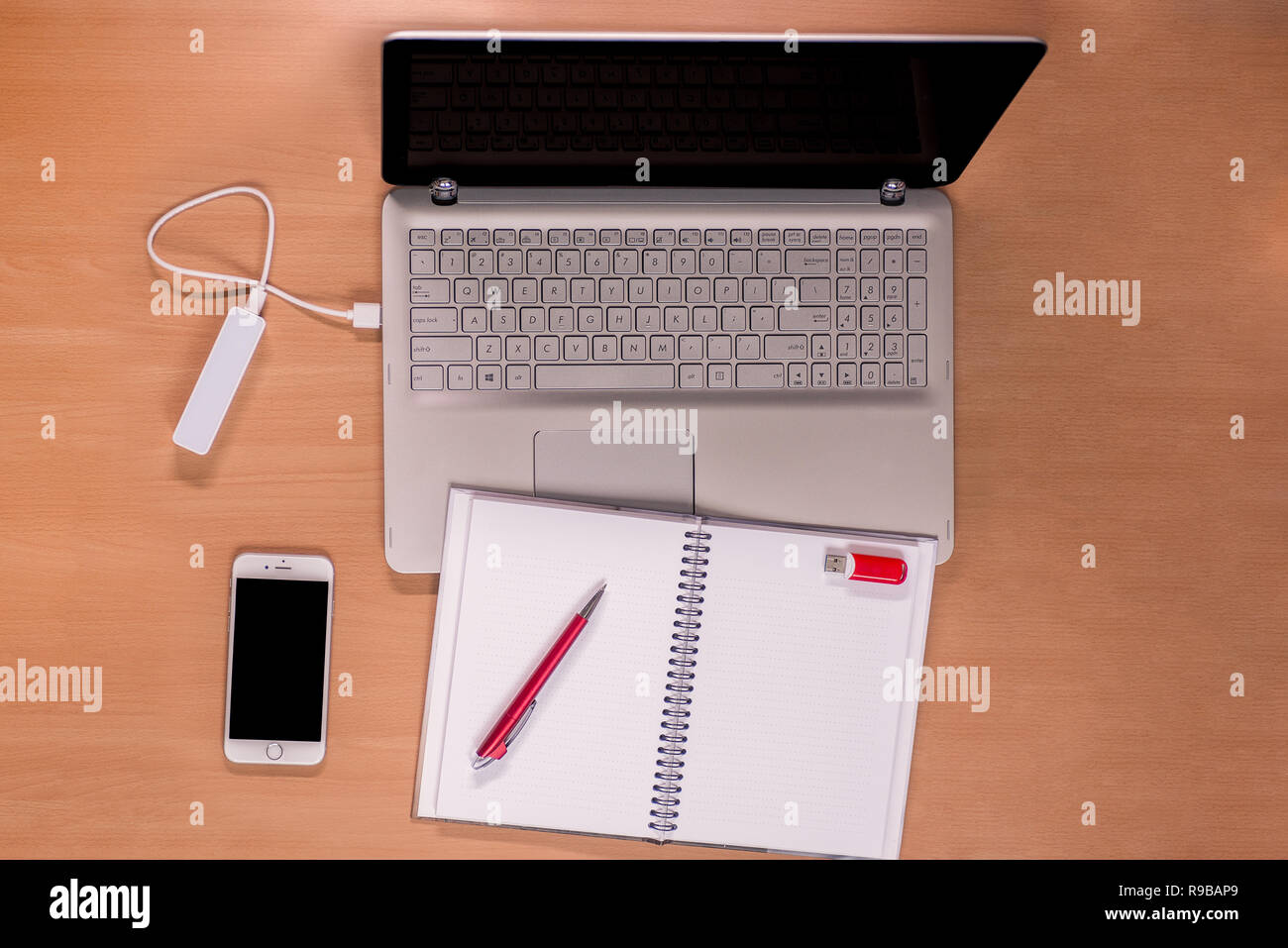Tecnologia per il business quotidiano sulla scrivania: Notebook aperto con power bank di ricarica, telefono cellulare e notebook vuoto aperto con penna rossa e memory stick Foto Stock