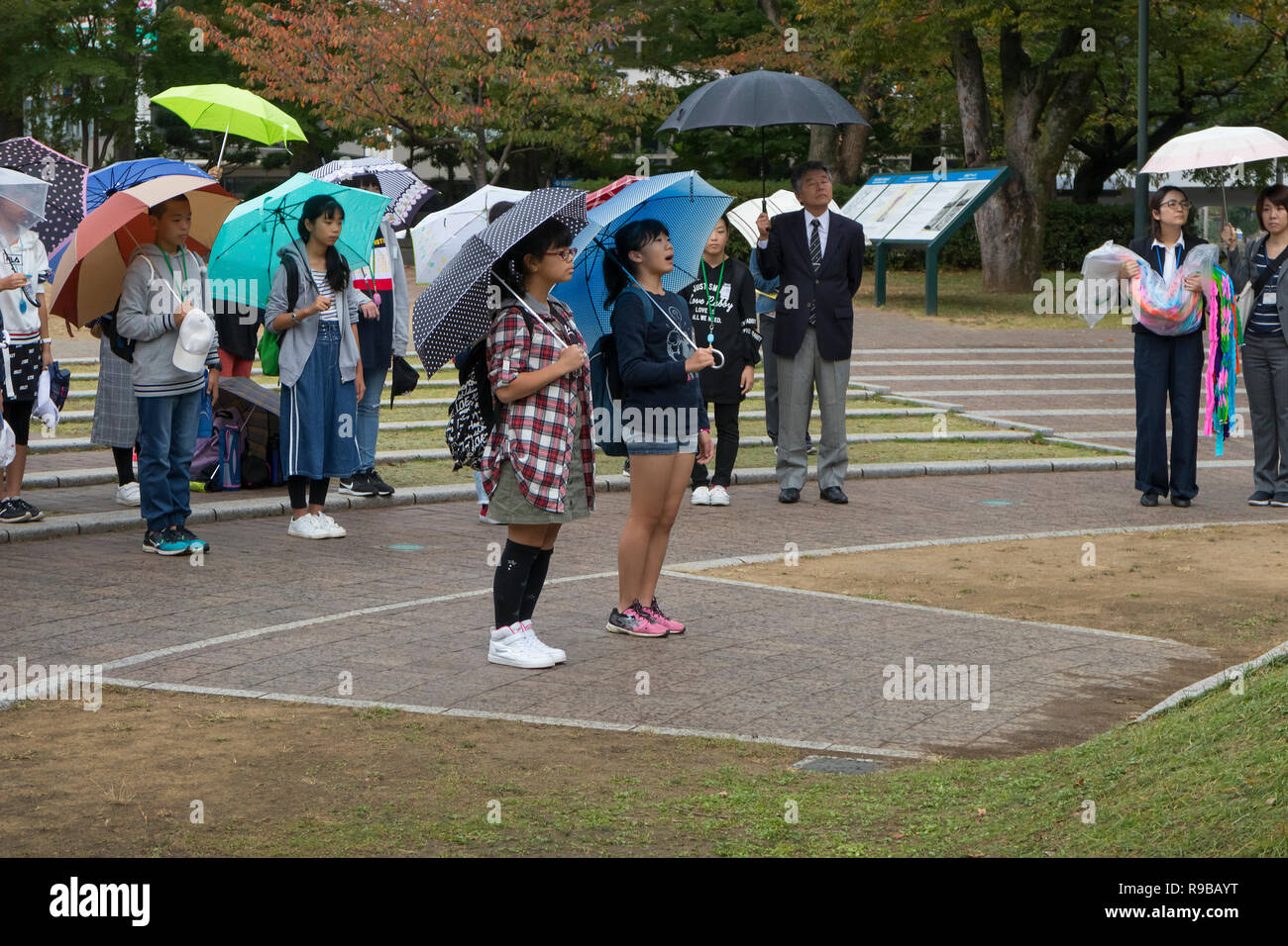 Nagasaki, Giappone - 23 Ottobre 2018: gli studenti a parlare e pagare rispetto a Nagasaki bomba atomica monumento sotto la pioggia Foto Stock