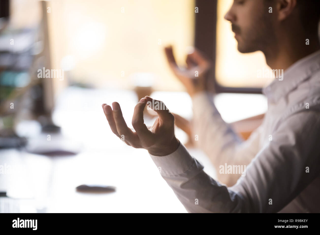 Uomo seduto alla scrivania tenendo le mani nel mudra meditando, primo piano Foto Stock