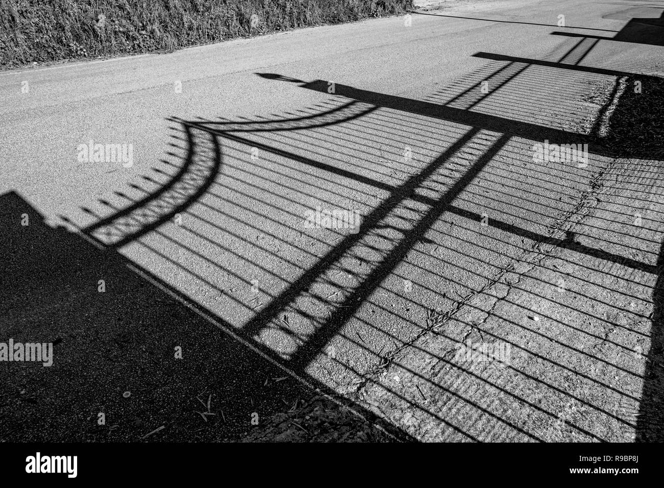 Ombra di bellissimi letti in ferro battuto con giardino recinto sul polverosa strada pubblica nella primavera del pomeriggio a Corfù, Grecia. Bianco e nero immagine di viaggio Foto Stock