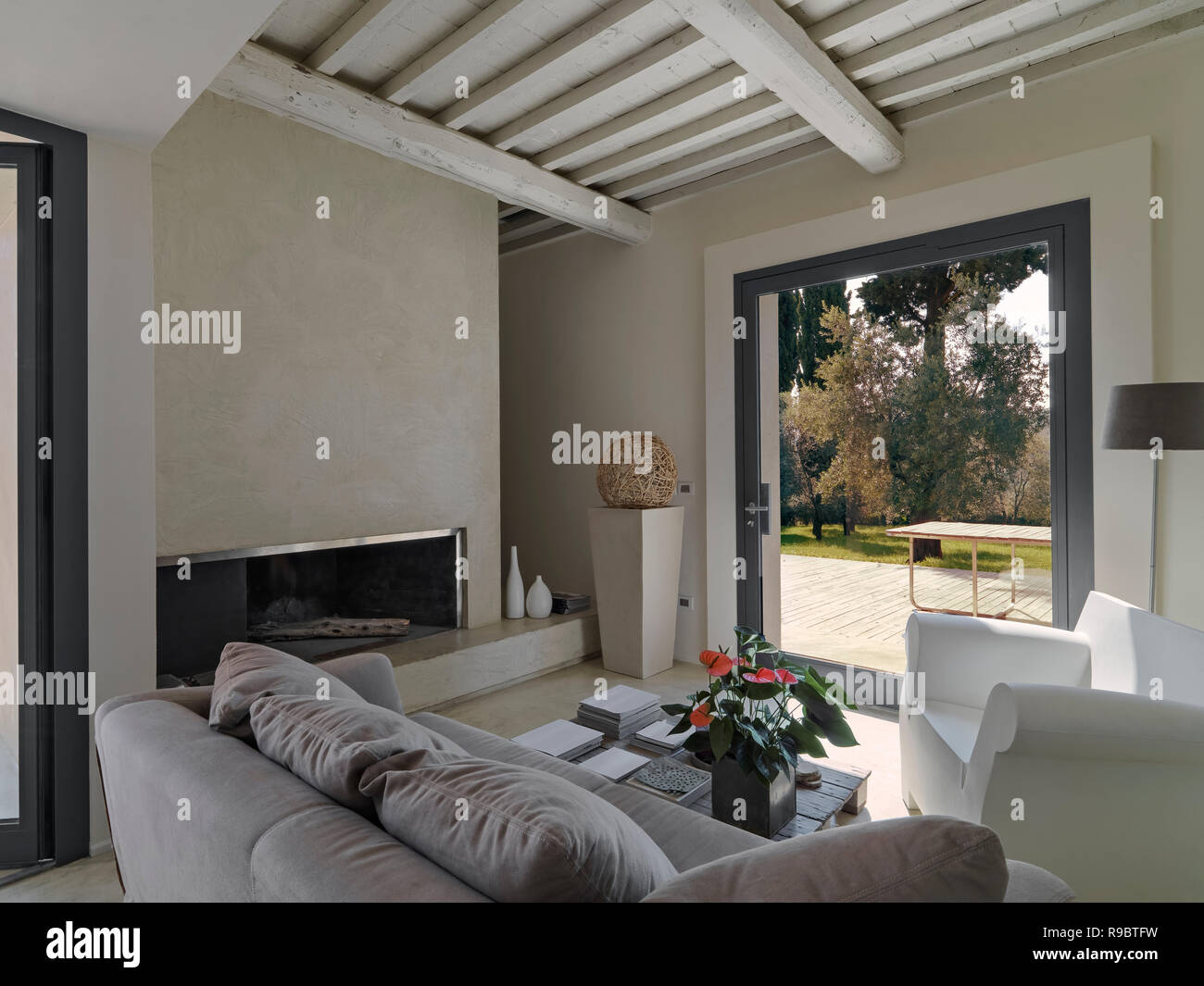 Scatti di interni di un moderno salotto con divani e poltrona davanti ad un camino che si affaccia sul giardino Foto Stock
