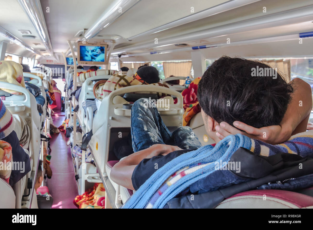 Reportage girato dell uomo guardando la TV a lunga distanza sleeper bus in Asia, di giorno Foto Stock