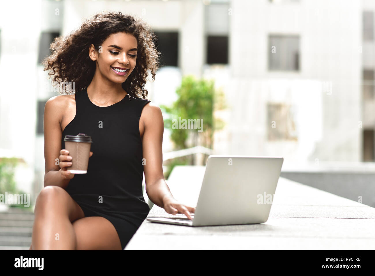 Giovani attraenti razza mista ragazza con bellissimi capelli afro che sorride guardando il suo schermo portatile durante la chiamata video. Giovane donna utilizzando laptop. Foto Stock