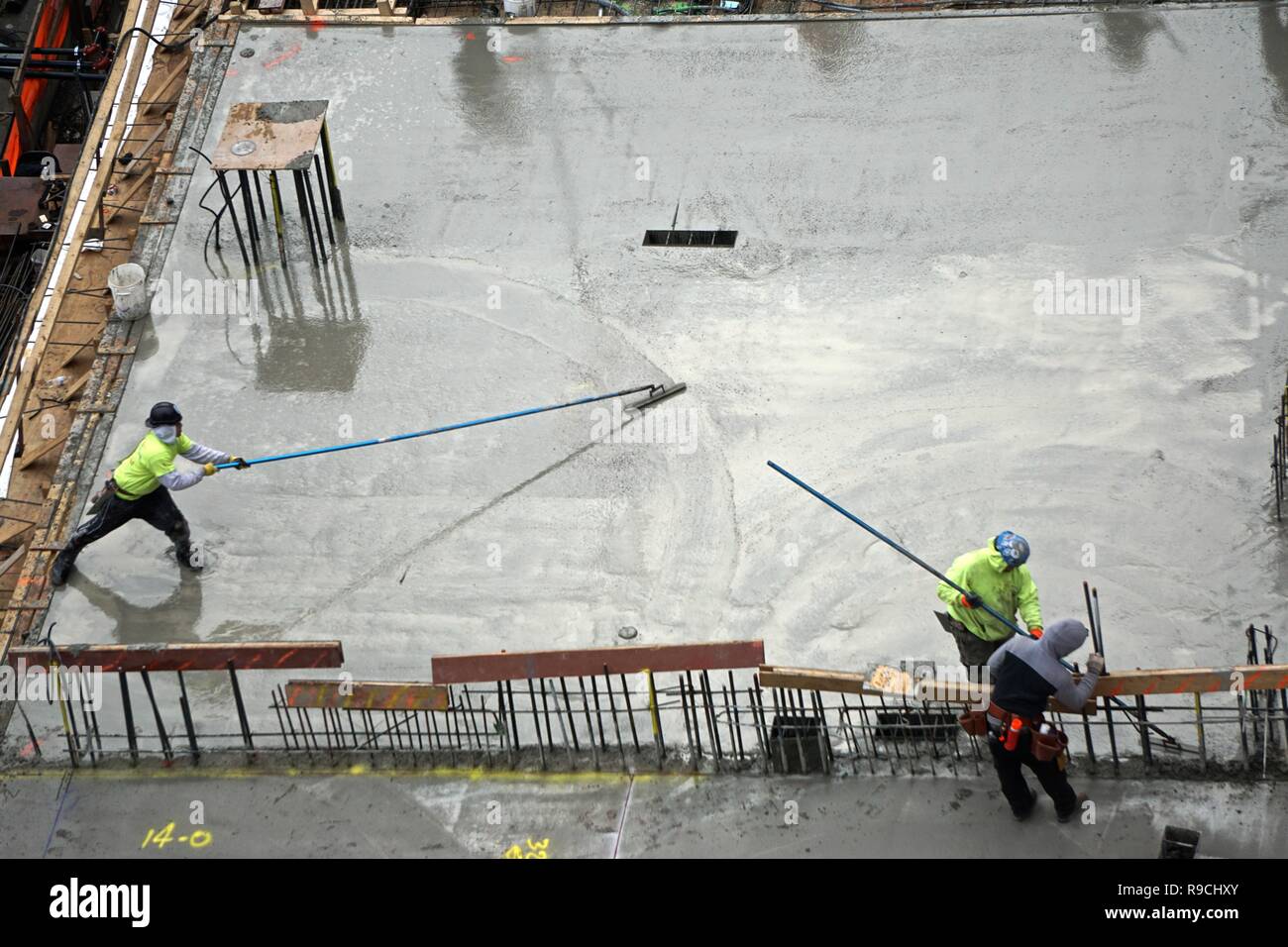 Operai utilizzare a lungo gestito strumenti per diffondere concreto nella costruzione di un 42-storia ad alto edificio di appartamenti nel centro di Manhattan, New York City. Foto Stock