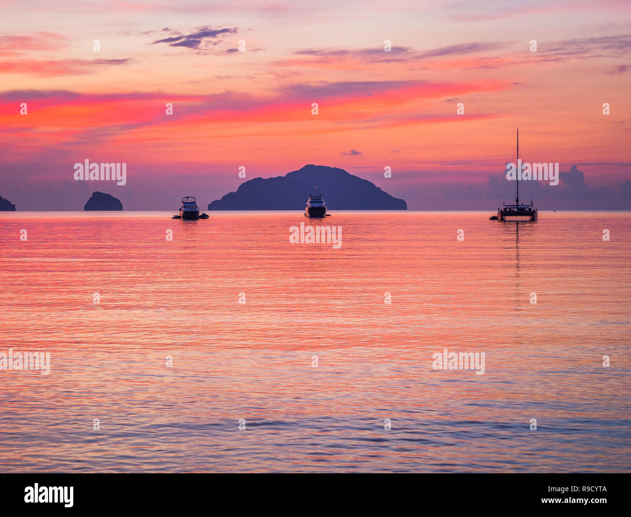 Tre barche ormeggiate nella tranquilla baia al tramonto, red sky, calma scena, perfetto per lo sfondo Foto Stock