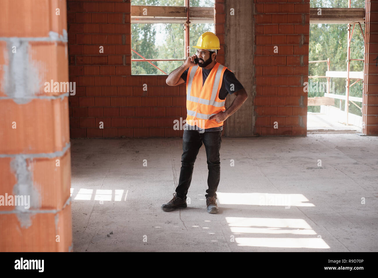 Uomo al lavoro nel cantiere sorridente e utilizza lo smartphone Foto Stock