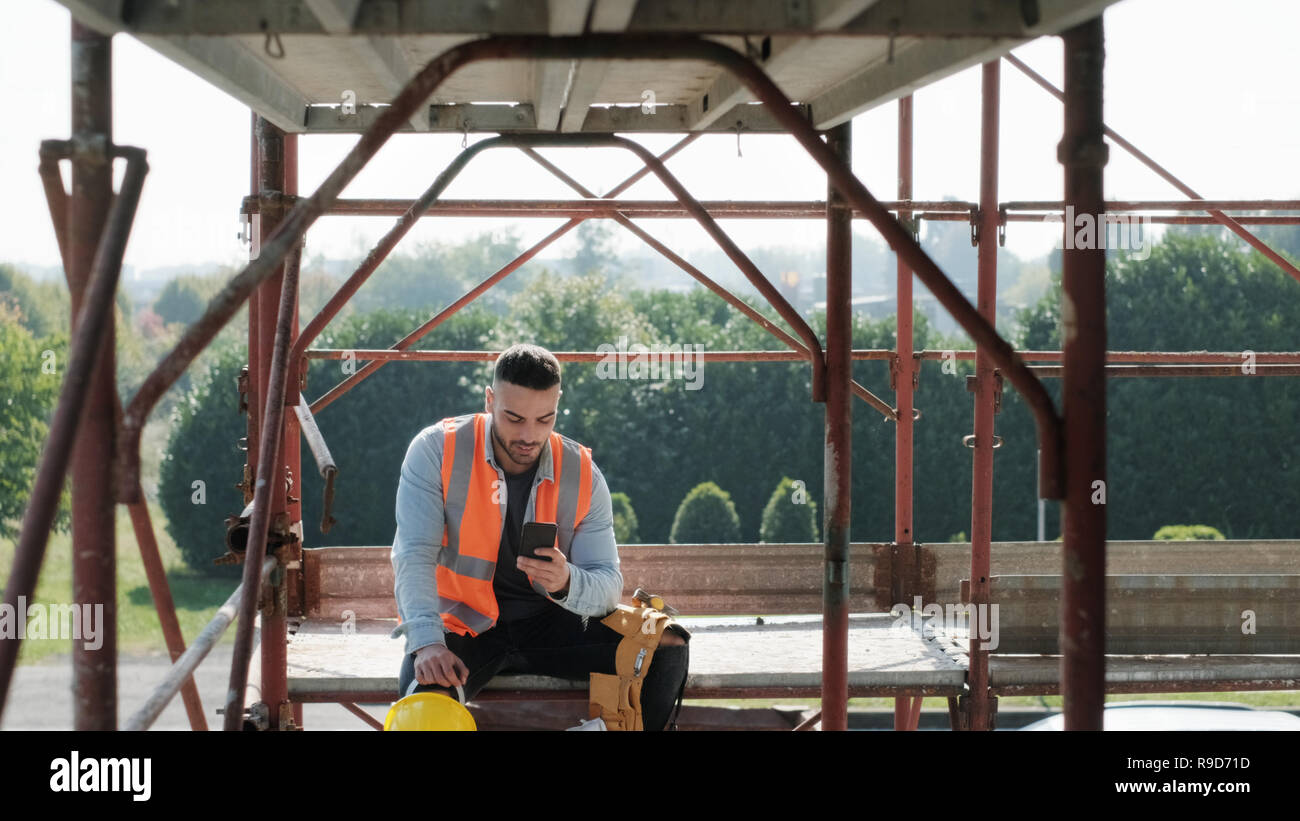 Uomo al lavoro nel cantiere sorridente e utilizza lo smartphone Foto Stock