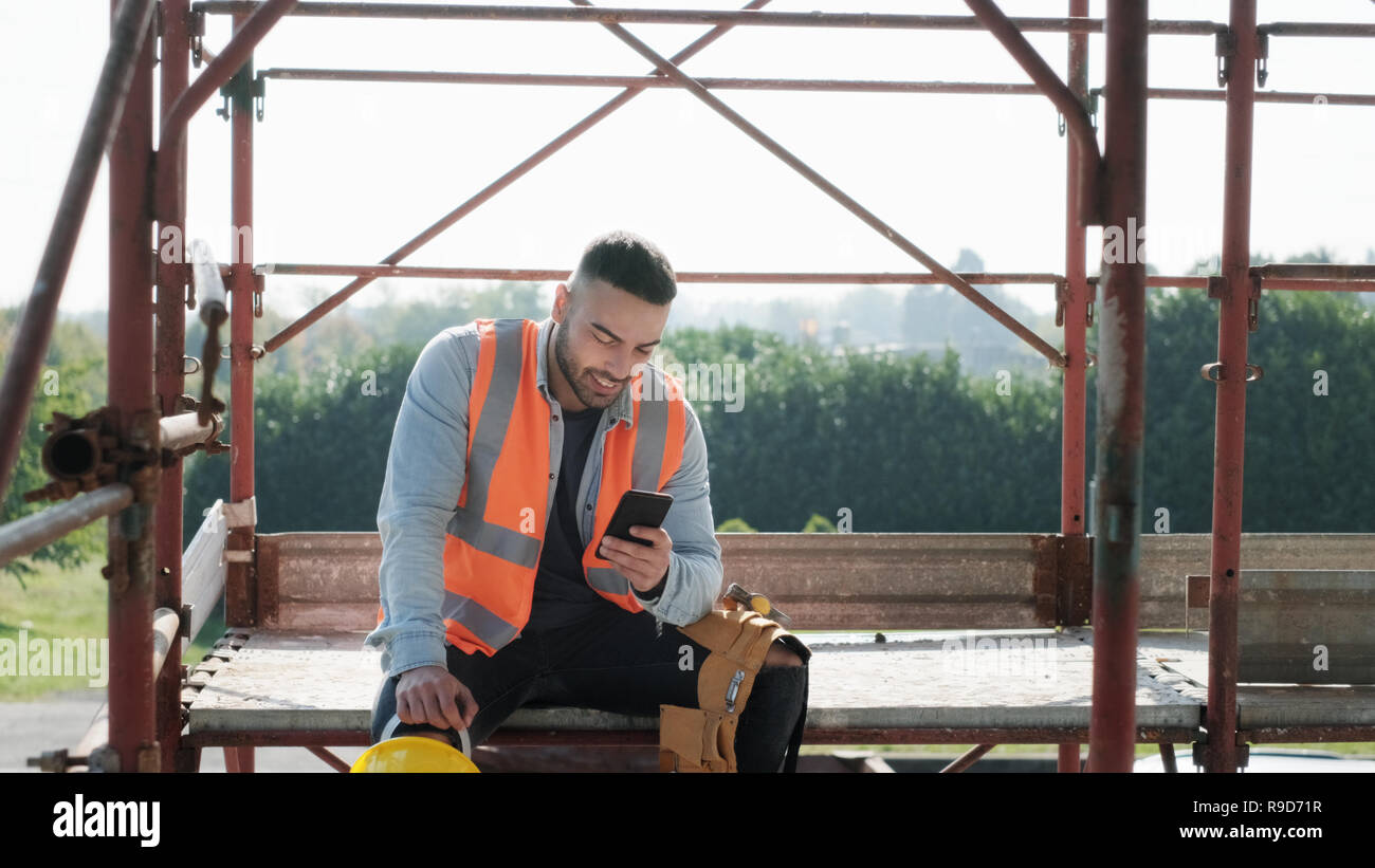 Uomo al lavoro nel cantiere sorridente e utilizza lo smartphone Foto Stock