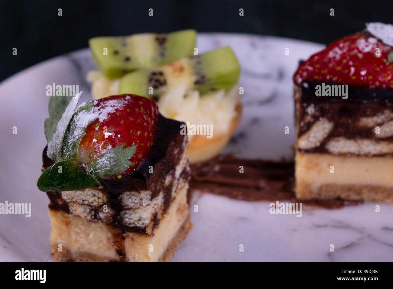 Tiny tortina con kiwi, panna montata e torta al cioccolato su un marmo nero tabella Foto Stock