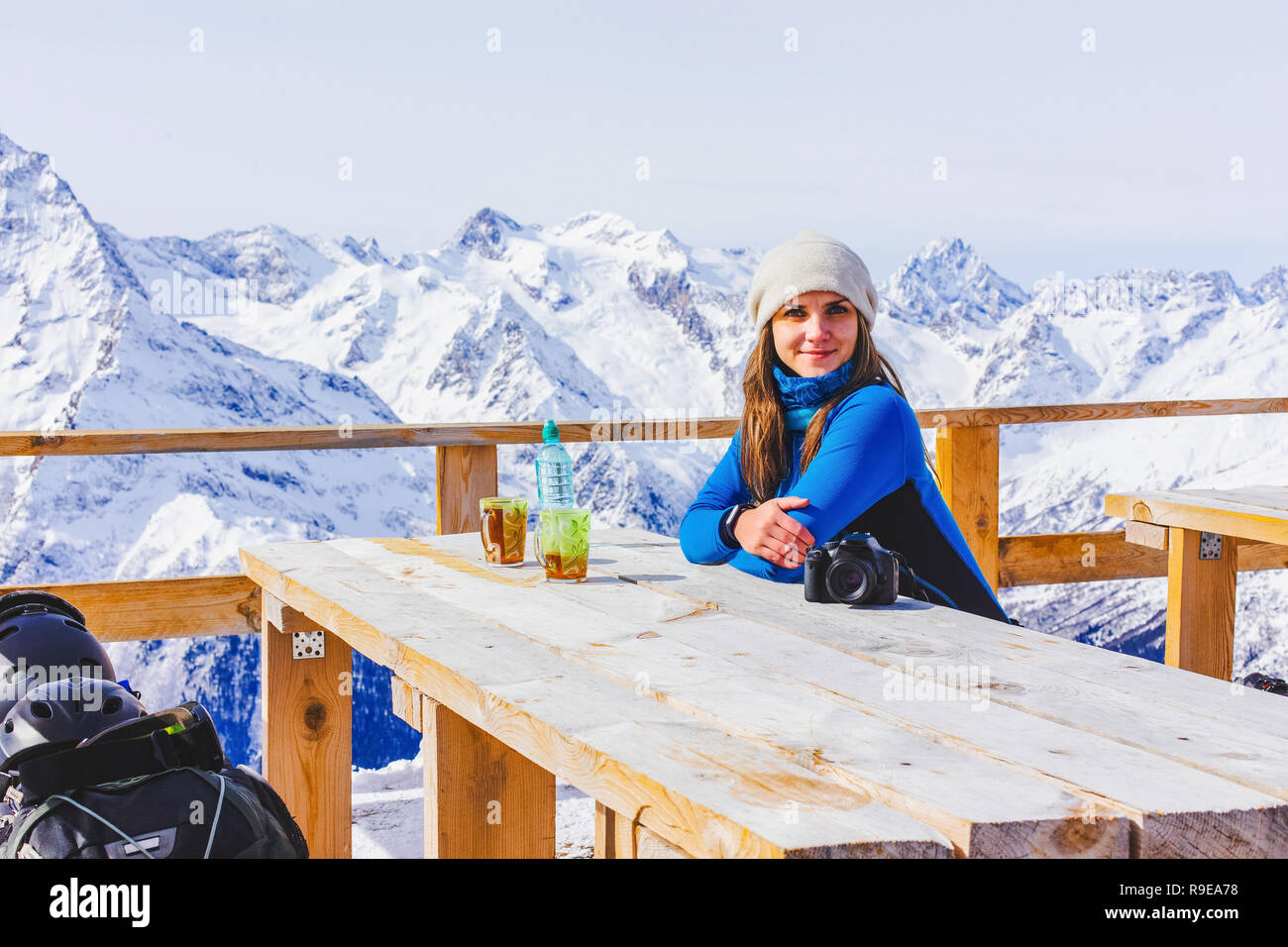 Donna snowboarder rilassante nella rustica terrazza in legno sulla montagna, inverno panorama alpino picchi innevati. Stile di vita viaggio avventura concetto, sport outdoor Foto Stock