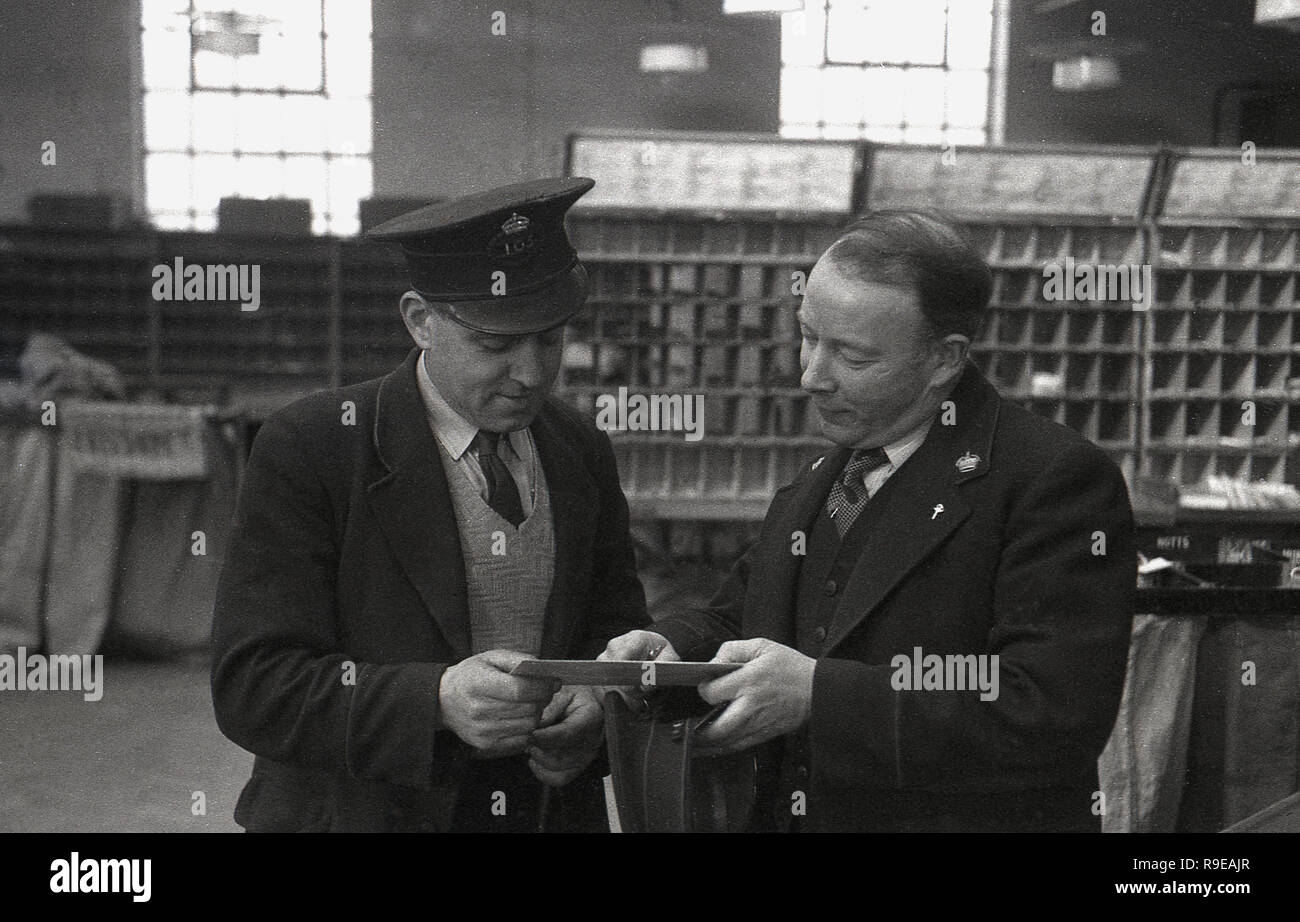 1948, l'immagine mostra due dipendenti GPO (Royal mail) in uniforme all'interno di un ufficio di smistamento postale, Inghilterra, Regno Unito. Un postino con un cappuccio in piedi con il suo supervisore che controlla l'indirizzo su una lettera. Foto Stock