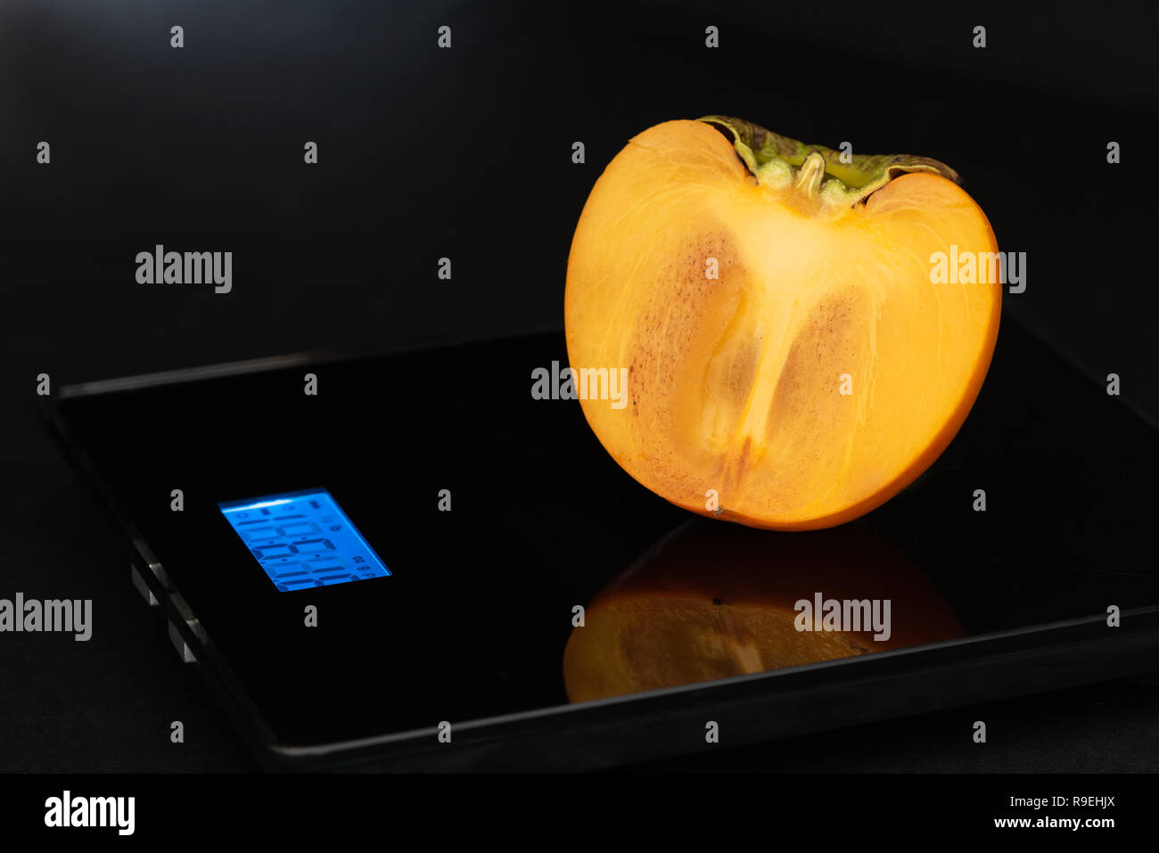 La metà di persimmon è su un sistema elettronico di peso su uno sfondo nero. Foto Stock