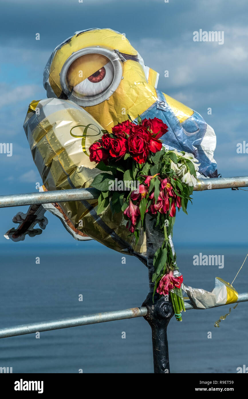 Minion palloncino elio con sguardo vigile e fiore memorial fissato a ringhiera Foto Stock