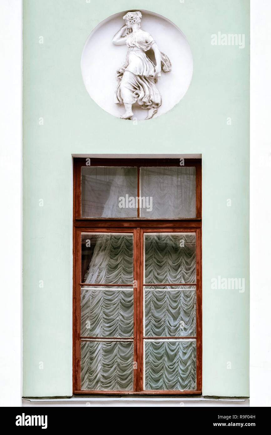 Una finestra rettangolare con un marrone telaio di legno contro il muro grigio della casa con un bassorilievo di una statuetta in una nicchia circolare. Da una serie o Foto Stock