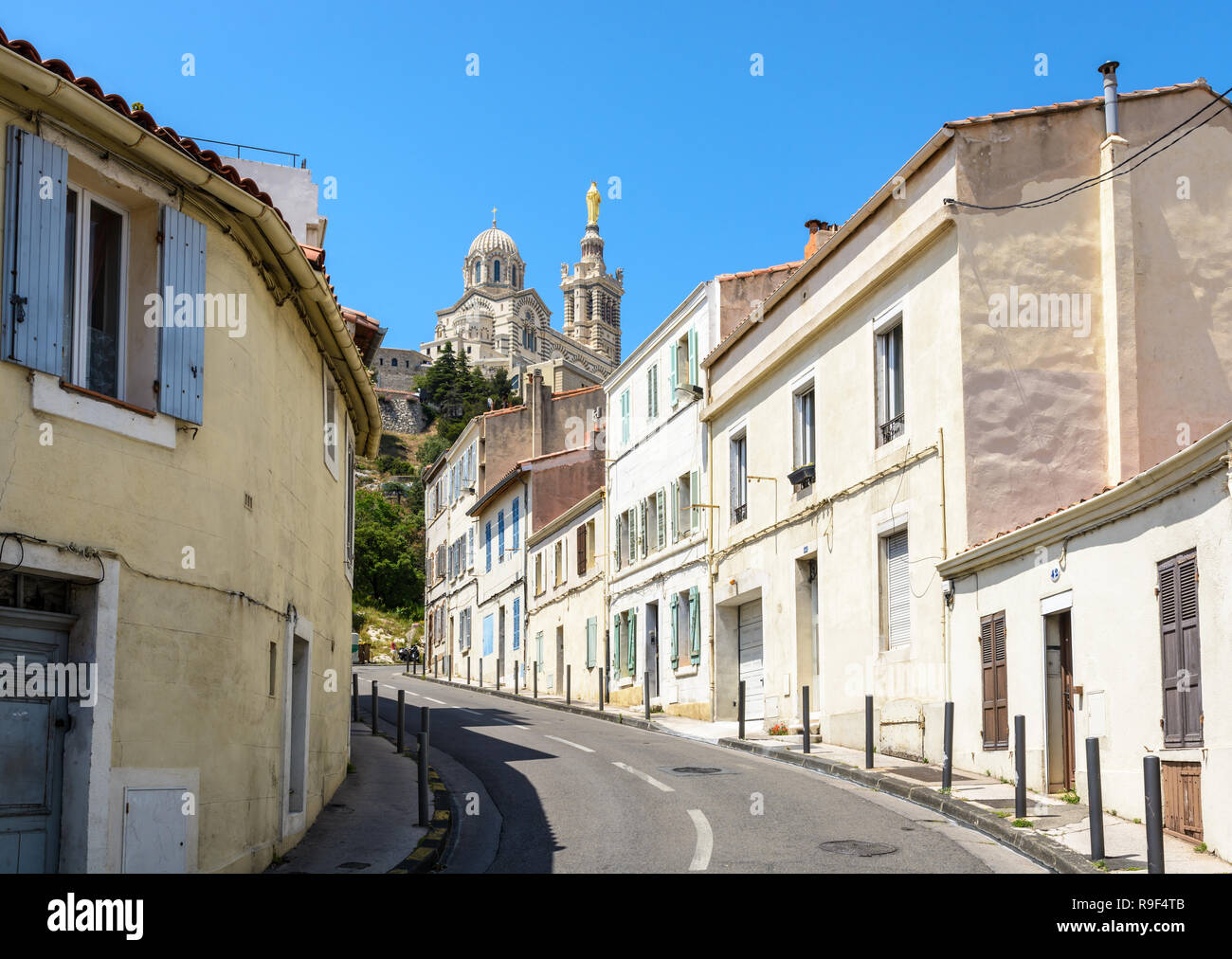 Una stretta strada in pendenza confina con vecchie case a schiera a Marsiglia, Francia, andando fino a Notre Dame de la Garde basilica sulla sommità della collina. Foto Stock