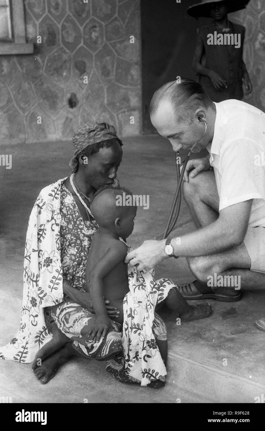 Western medico esaminando giovane ragazzo africano anni cinquanta persone native, Africa occidentale Foto Stock