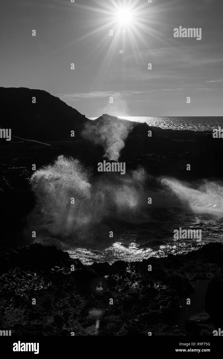 Retroilluminazione dell'acqua che viene espulsa da un foro nella roccia quando le onde si infrangono in Spouting Horn Foto Stock