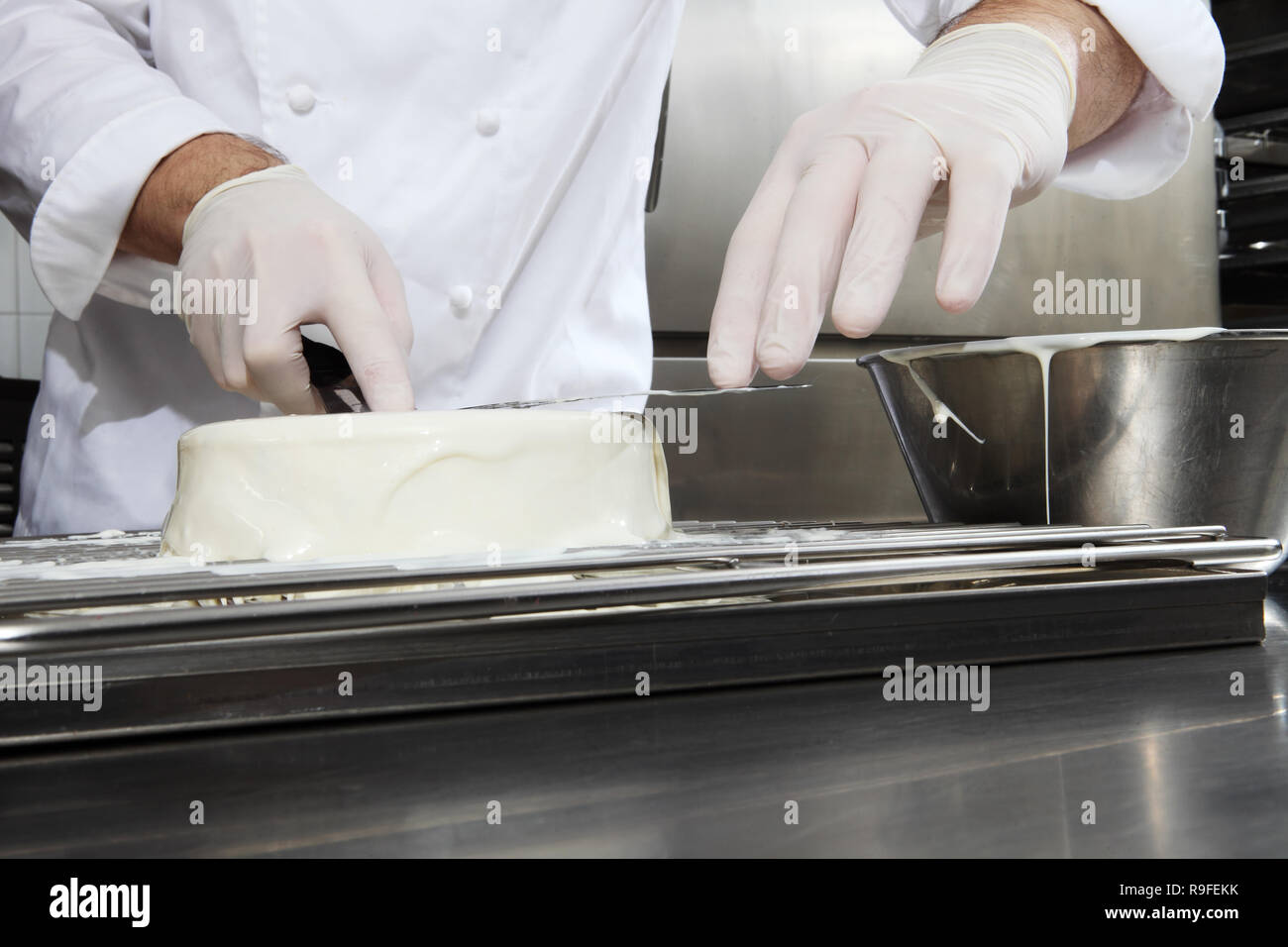 Mani pastry chef prepara una torta, coprire colata di glassa bianca, lavorando su un acciaio inossidabile cucina industriale piano di lavoro Foto Stock