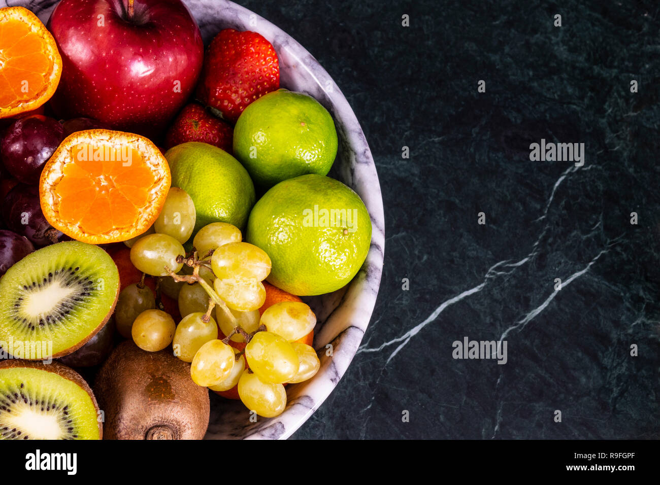 Fresco tropicale fruitson nella ciotola sul marmo nero lo sfondo. Ananas, papaya, mango, kiwi, uva, granato, tangerini, banane, mele, anguria sli Foto Stock