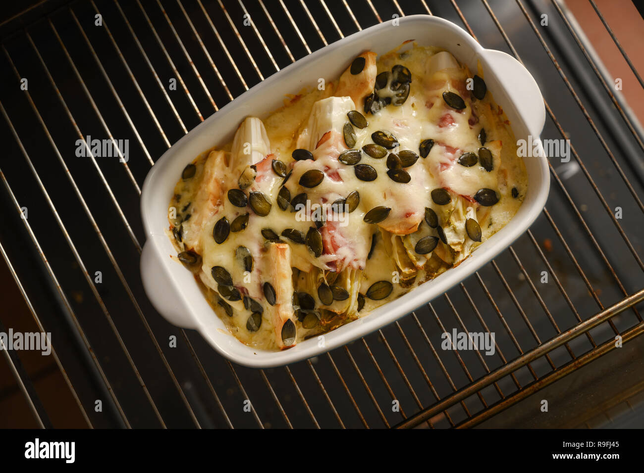 Indivia o cicoria al gratin con Apple, prosciutto, formaggio e i semi di zucca in una casseruola su una griglia da forno dolce da forno Foto Stock