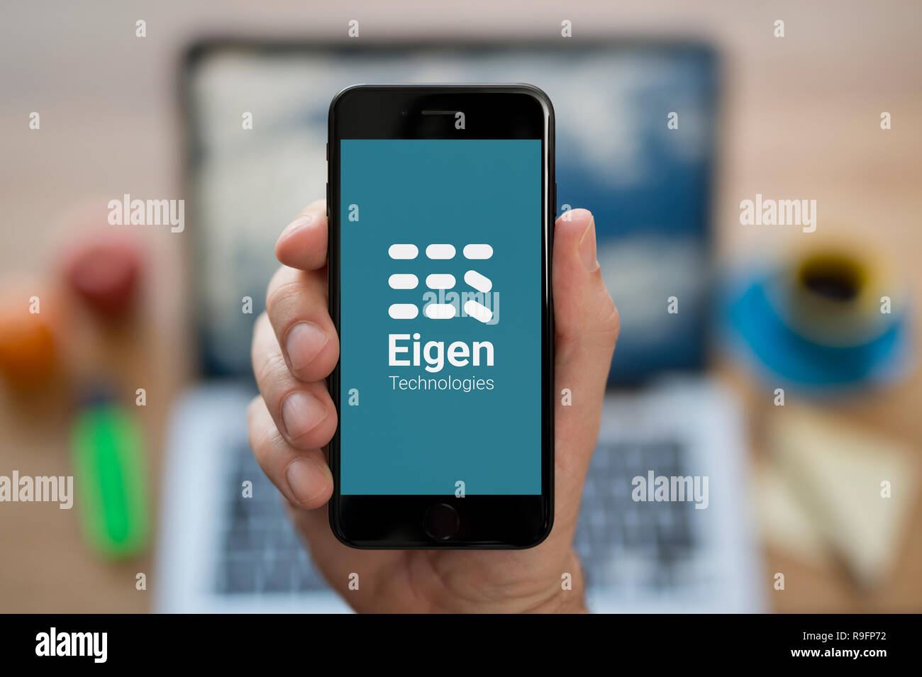 Un uomo guarda al suo iPhone che visualizza le tecnologie Eigen logo (solo uso editoriale). Foto Stock