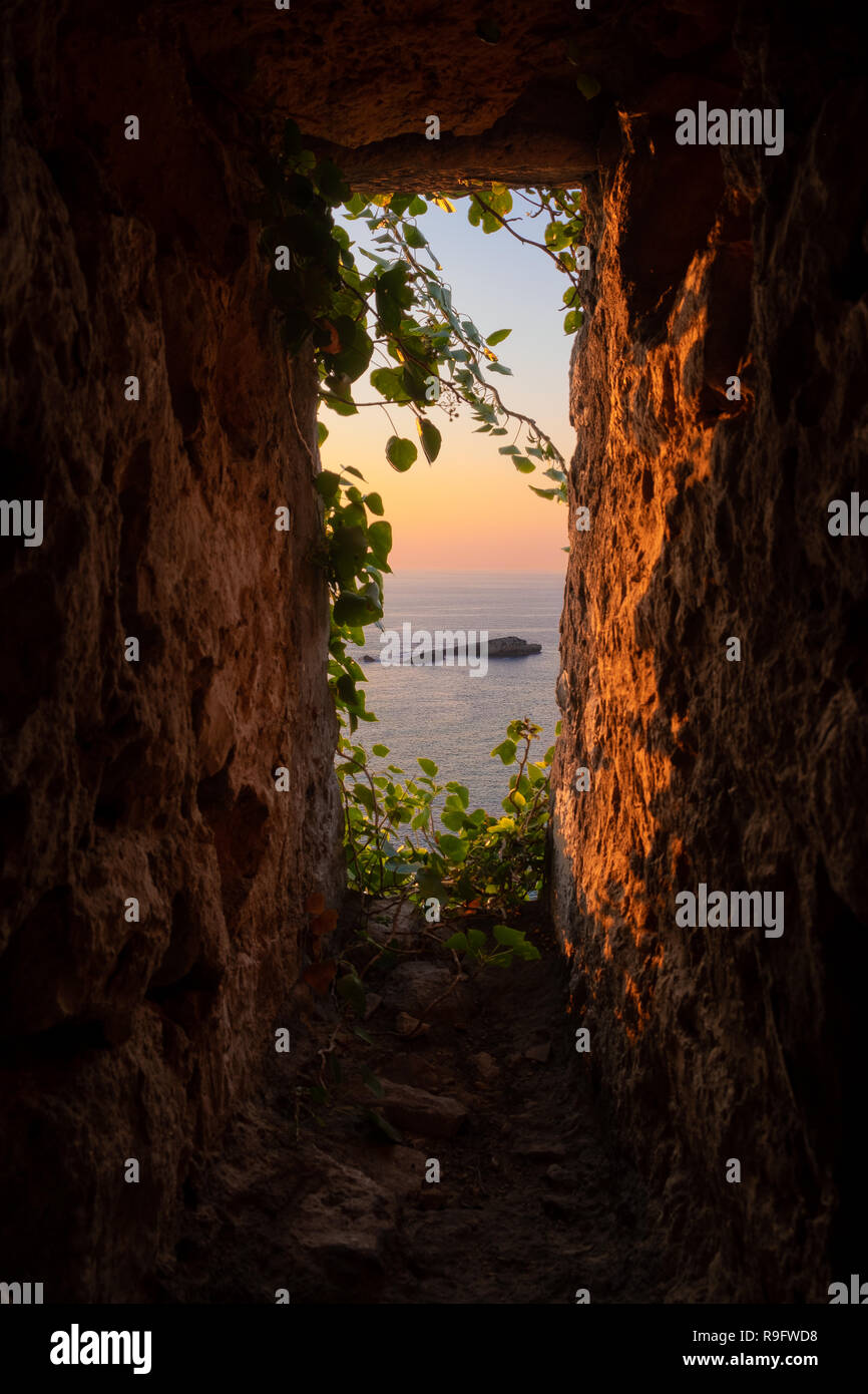 Idillica vista al tramonto di una piccola isola rocciosa dalla finestra fortezza illuminata dal sole dorato, con ivy crescendo in, Ulcinj Montenegro Foto Stock