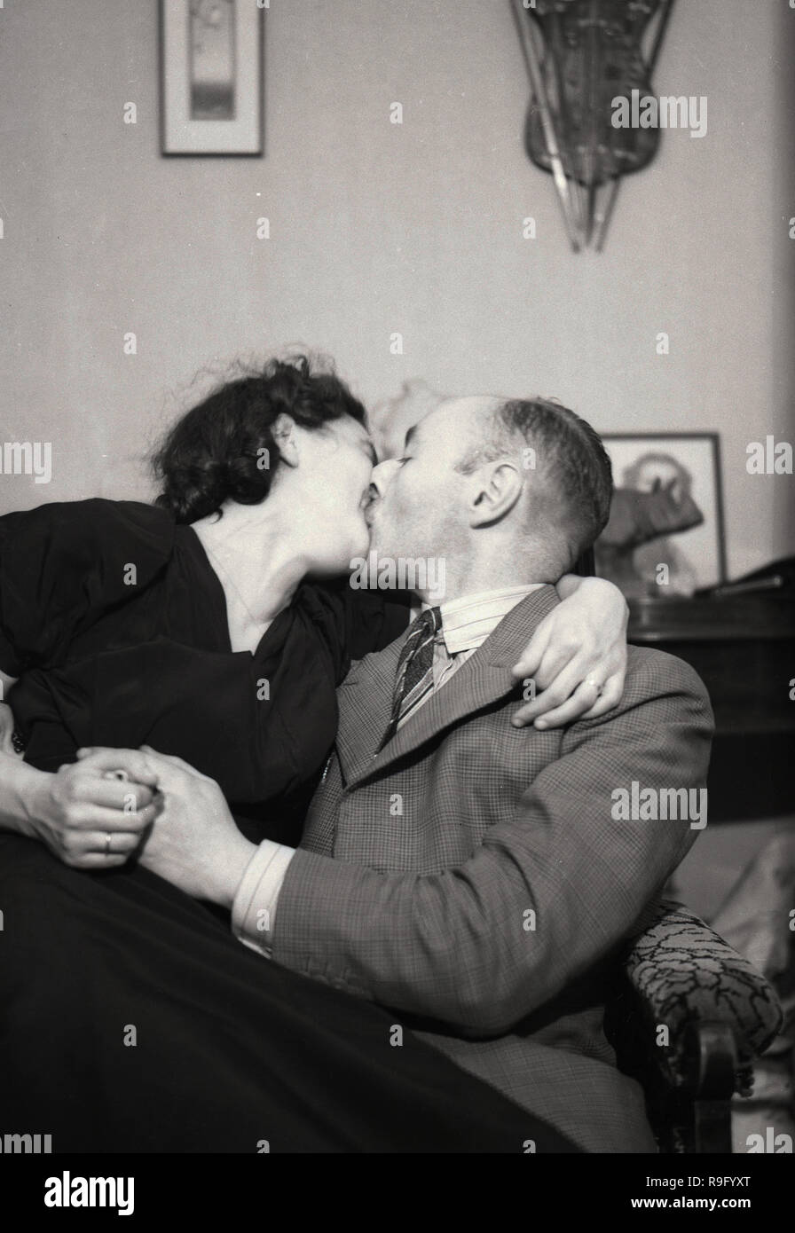 Degli anni Cinquanta, un paio di baciare, un uomo anziano con una giovane donna seduta insieme su una sedia che abbraccia, Inghilterra, Regno Unito. Foto Stock