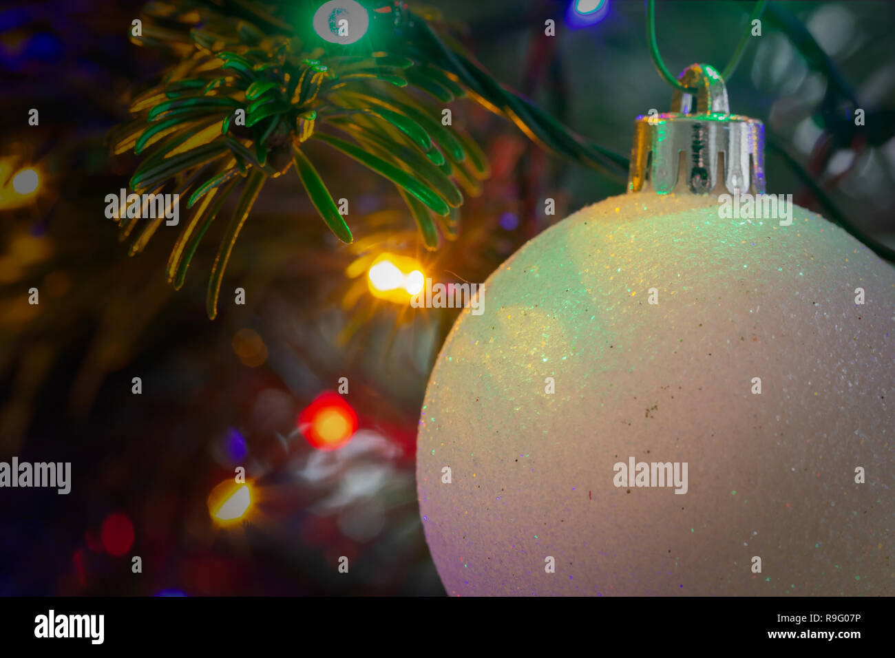 Close up di un bianco, frosty ninnolo davanti a luci colorate su di un albero di Natale Foto Stock